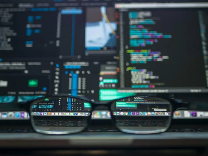 Lines of code reflected through eyeglasses on a laptop screen, symbolizing developer focus and attention to detail
